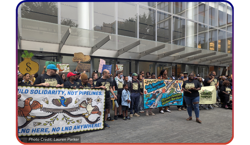 a photo of racially and intergenerational diverse group of climate activist holding signs and banners outside of a corporate building.